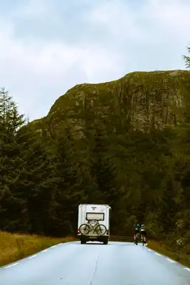 A camper besides a biker on a road with a big mountain in the back.